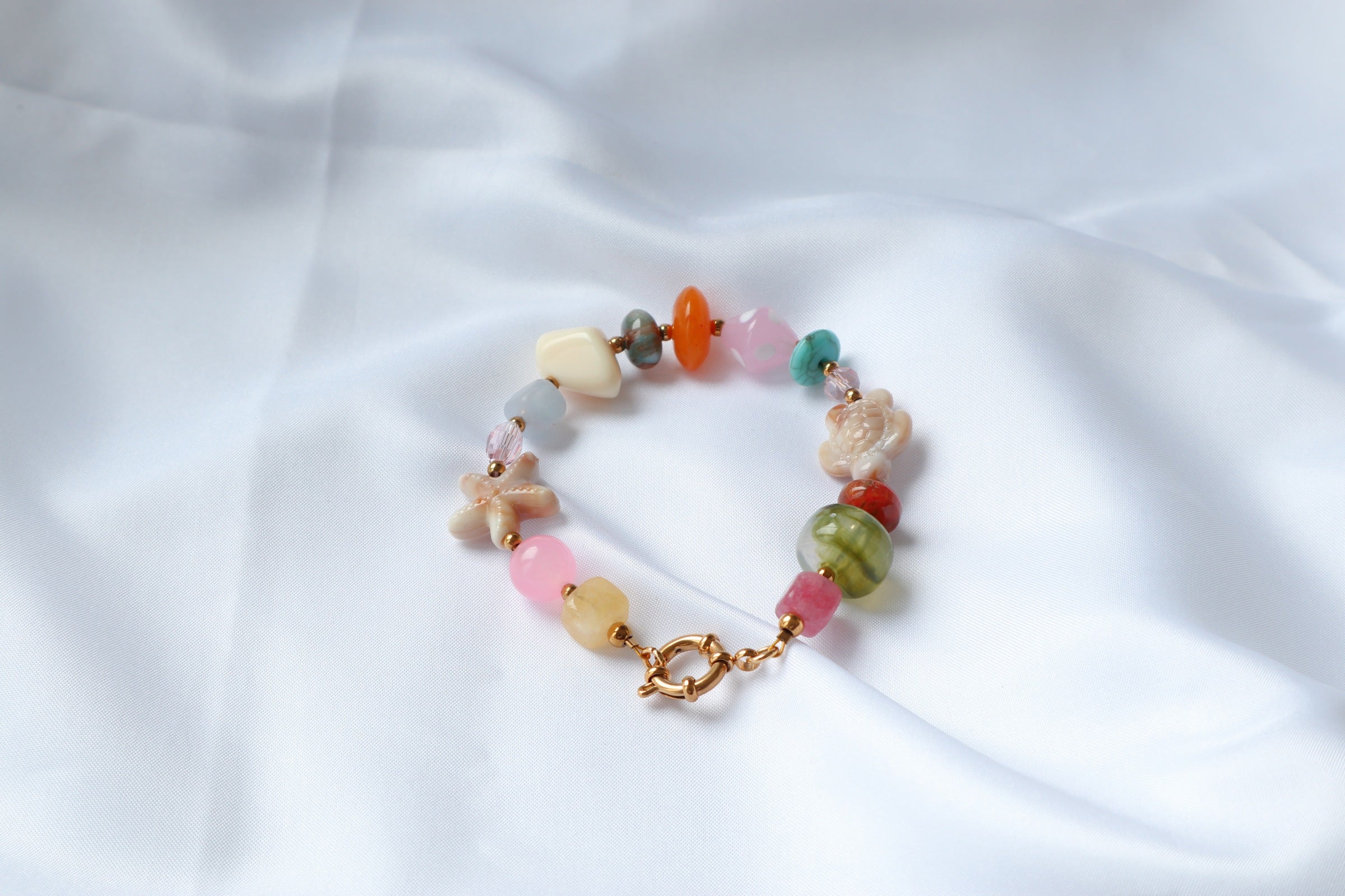 Handgemaakte armband Norah met glaskralen, resin en natuursteen in pastelkleuren met goudkleurige toggle sluiting